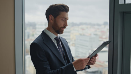 Depressed middle-aged investor checking financial paperwork near office window close up. Bearded businessman reading documents feeling stressed about banking loan. Man auditor worried about payments.の写真素材