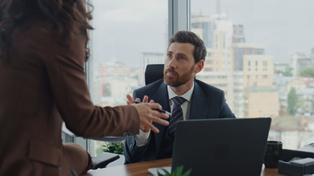 Happy relaxed coworkers communicating in office sitting desk close up. Confident businesswoman sharing new ideas with bearded colleague. Bearded company employee manager working laptop in elegant suitの写真素材
