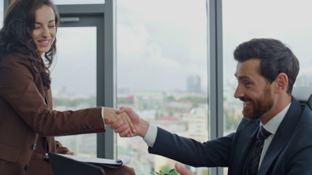Happy corporate partners shaking hands agreeing joint project sitting at office desk close up. Confident coworkers smiling satisfied successful partnership. Couple friendly colleagues working togetherの写真素材