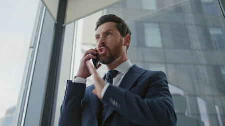 Angry boss shouting arguing in phone call close up. Furious businessman ending conversation standing in modern office. Stressed ceo manager reacting emotionally on bad news company crisis work fail.の写真素材