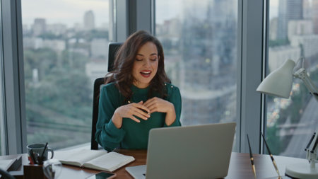 Brunette ceo talking on online conference using internet connection sitting at luxury office. Attractive business woman conducting business video meeting. Lady boss explaining work issues to webcamの写真素材