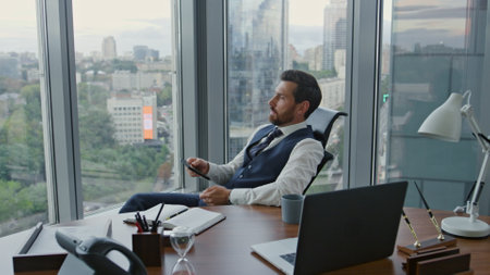 Disappointed manager reading message on smartphone sitting at luxury office with panoramic window....
