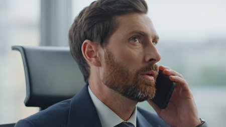 Confident man professional lawyer talking phone sitting modern office close up. Bearded business owner negotiating on smartphone feeling dissatisfied with work results. Project manager finishing talk.の写真素材