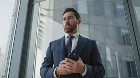 Upset businessman worried after phone call standing near office window close up. Stressed financial specialist finish telephone conversation dissatisfied company results. Manager feeling unsuccessful.の写真素材
