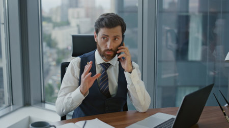 Smart bearded entrepreneur talking smartphone during working on laptop. Confident serious business man having phone negotiation sitting at office desk. Ceo manager noting in notebook at mobile call.の写真素材