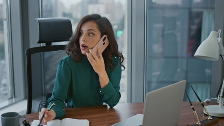 Busy attractive businesswoman giving orders by phone call sitting modern office desk. Confident successful woman ceo manager working in luxury workplace talking smartphone. Lady boss speaking mobile.の写真素材