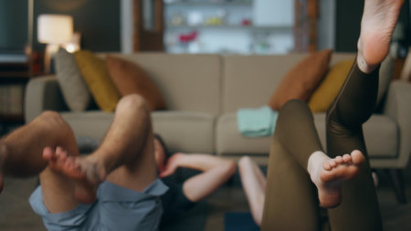 Closeup legs spinning training fitness in apartment. Young sporty couple lying on sport mat with feets up moving like bicycle at home. Fit millennial family workouting together. Healthy lifestyle.の写真素材