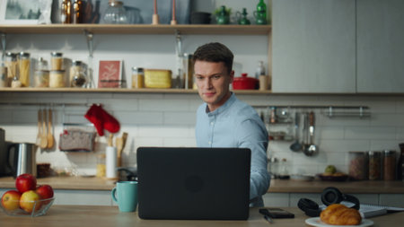 Positive man turning on cooking video lesson preparing breakfast at modern kitchen. Attractive guy cooking food alone using online recipe on laptop. Smiling man have fun making healthy meal.の写真素材