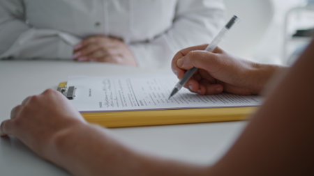 Unknown woman filling form for cosmetic procedures sitting at desk with clinic specialist close up....