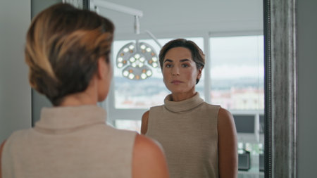 Portrait of woman looking mirror after beauty procedures in luxury cosmetology clinic. Attractive lady checking skincare results at beautician visit close up. Aesthetic therapy in modern beauty salon.の写真素材