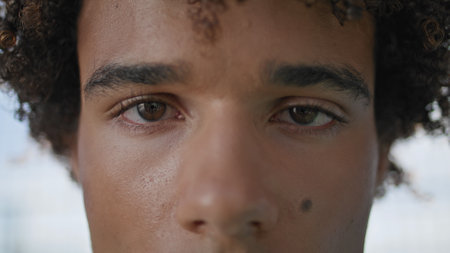 Focused guy staring lens outdoors extreme closeup. Curly hair model eyes looking camera directly at street macro portrait. Handsome student with attractive deep sight. Serious teenager posing outdoorsの写真素材