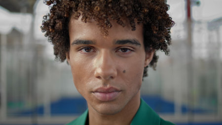 Serious teen staring lens outdoors closeup. Boldly model posing next to stadium background. Curly...