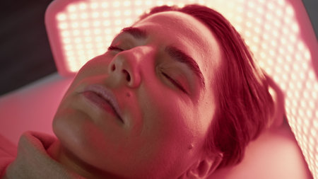 Attractive woman relaxing under led light on photodynamic procedure close up. Clinic client lying on phototherapy non-invasive painless effective facial rejuvenation. Aesthetic medicine concept.の写真素材