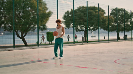Sportive man practicing street basketball alone. Focused afro hairstyle guy making attempt to score goal at stadium. Serious streetball player training outdoor at urban playground. Summer lifestyleの写真素材
