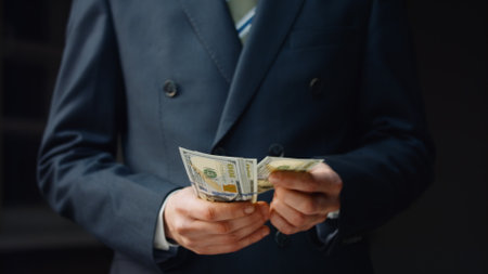 Smiling successful business man counting cash hundreds dollars close up. Middle-aged bearded manager calculating investment profit wearing black elegant suit. Office worker satisfied money income.の写真素材