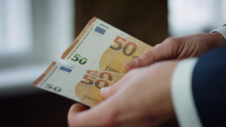 Unknown businessman holding pack of euro bills indoors close up. Man hands counting european currency banknotes. Young manager calculating money cash. Business profit finance income economy concept.の写真素材