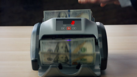 Modern counter counting dollar bills close up. Man hand putting wad american hundred banknotes into electronic bank equipment for calculation paper currency. Automatic machine calculating money cashの写真素材