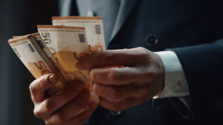 Closeup man hands counting money denomination of fifty euro indoors. Unknown businessman in elegant black suit calculating cash american currency from business investment. Financial success concept.の写真素材