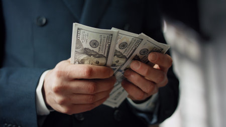 Businessman hands counting pack of american dollars close up. Unknown owner in luxury suit...