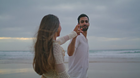 Cheerful lovers connecting hands at dark beach closeup. Smiling pair touching arms on evening ocean side. Romantic couple interlacing fingers on cloudy nature date. Loving people spend time togetherの写真素材