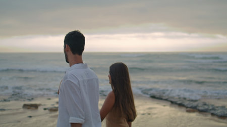 Lovely family holding hands at misty ocean closeup. Happy woman man walking on dusky beach. Affectionate sweethearts enjoying each other at foggy sea shore. Young couple spending honeymoon togetherの写真素材
