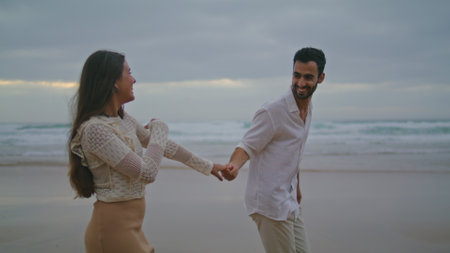 Playful pair talking dark ocean closeup. Positive lovers holding hands on evening sea coast. Romantic partners enjoying date on cloudy nature. Two loving people spend time together. Leisure conceptの写真素材