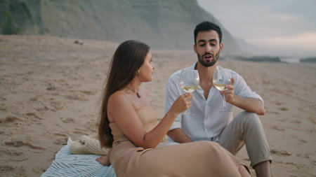 Romantic couple celebrating vacation at seashore. Positive family holding wineglasses drinking alcohol at sandy beach picnic. Handsome man telling jokes to laughing woman. Spouses spending anniversaryの写真素材