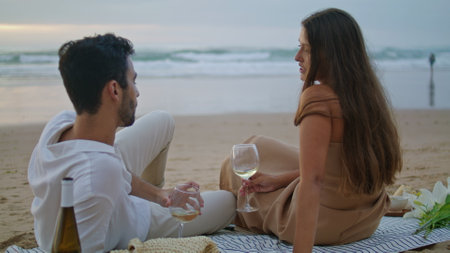 Sensual couple celebrating vacation at seashore. Romantic family clinking glasses at sandy beach picnic. Cute sweethearts drinking alcohol beverage back view. Spouses spending anniversary togetherの写真素材