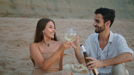 Smiling couple clinking wine glasses at beach picnic closeup. Happy new family celebrating honeymoon date together at sandy nature. Positive lovers drinking alcohol beverage near ocean at cloudy dayの写真素材