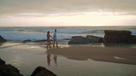 Affectionate couple going sea shore wide shot. Loving woman looking man on cloudy sky beach. Married people watching ocean horizon. Love sweethearts enjoying romantic time together. Feelings conceptの写真素材