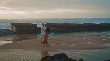 Beautiful couple enjoy sea beach. Happy people spinning together on cloudy day. Romantic boyfriend girlfriend embracing by ocean waves. Cheerful rejoicing pair celebrate love outside. Holiday conceptの写真素材