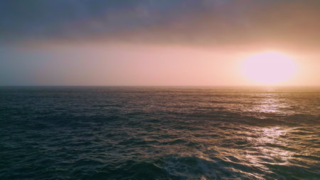 Amazing orange coastal sunset over beautiful ocean waves aerial view. Picturesque golden cloudy sky at calm seascape. Sea water rippling reflecting sundown light in slow motion. Evening marine sceneryの写真素材