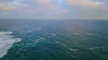 Cold gray ocean rippling under heavy cloudy sky drone view. Lonely ship floating in distance at deep dark sea water. Dangerous waves foaming rolling on rocky seashore super slow motion. Marine dusk.の写真素材