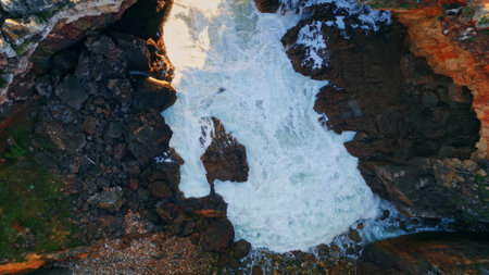 Powerful stormy sea waves crashing on volcanic seashore aerial view. Foamy white ocean water washing splashing at rocky summer coast in super slow motion. Rough cliffside with dangerous foaming surf.の写真素材