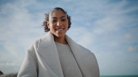 Cheerful woman open arms at cloudy sky bottom view. Happy african american pose enjoying triumph freedom outdoors. Smiling excited girl dreaming rejoicing in sunlight. Weekend leisure relaxation.の写真素材