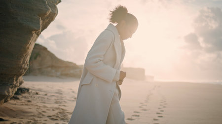 Serene woman resting beach play with sand in sunlight. Black hair tourist enjoy vacation at seashore. Focused sad african american thinking look inspiration at ocean. Female silhouette at empty shoreの写真素材