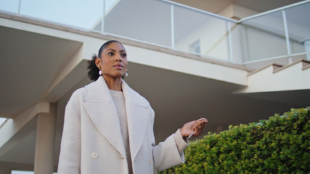 Confident woman walking street suburbs. Gorgeous african american realtor hold keys stroll neighborhood. Stylish businesswoman commute home in evening. Real estate agent landlord go to client meetingの写真素材