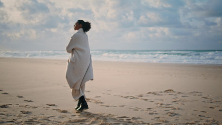 Calm traveler walk beach on autumn weekend. Lonely african american admiring nature watch waves rear view. Peaceful black hair woman enjoy time alone contemplating life. Mindfulness balance conceptの写真素材