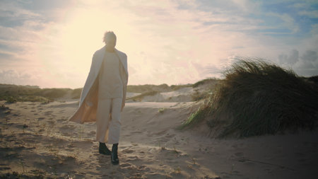 Woman resting sand dunes posing in sunlight. Stylish african american admiring wild seaside landscape relaxing on weekend trip. Confident curly model dream enjoying time alone. Serene calm femaleの写真素材