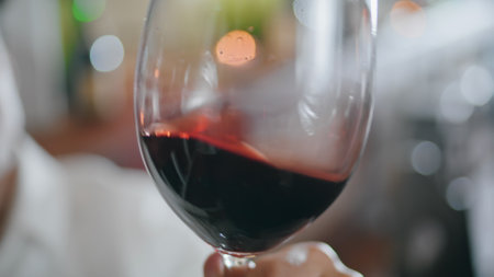 Taster hand holding crystal elegant glass with gourmet red wine shaking alcohol close up. Unrecognizable man sommelier swirling burgundy grape drink for checking color. Winemaking degustation concept.の写真素材