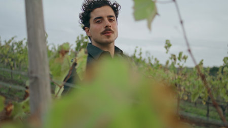 Happy relaxed vineyard worker walking between vine rows looking camera with smile close up. Young...