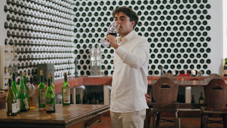 Professional young man winemaker making red wine sip from glass goblet tasting flavour gourmet drink. Italian sommelier drinking grape beverage at degustation in cozy winery cellar. Winemaking conceptの写真素材