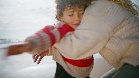 Playful boy running mother on ocean shore. Happy parent woman hug spinning child in autumn sunlight....