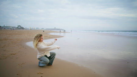Woman throwing stones water ocean on cloudy day. Thinking girl resting seaside contemplating life alone. Beautiful serene person tourist enjoying autumn weekend at sea. Dreamy peaceful mood concept.の写真素材