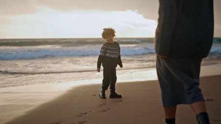 Kid mother walking sand beach leaving footprints on sunset. Joyful family play resting autumn shore together. Cute preschool boy enjoying game with babysitter. Single mom spending weekend with sonの写真素材