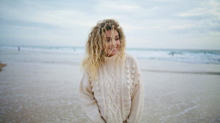 Happy woman enjoying ocean on cold autumn weather. Smiling lady walking shore in knitted sweater on spring weekend. Attractive blonde relaxing contemplating life outdoors. Serene calm people concept.の写真素材