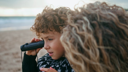 Closeup kid looking spyglass at ocean shore. Laughing family relaxing outdoors spending autumn weekend on beach. Happy single mother having fun playing with adorable curly son. Parent bonding momentsの写真素材