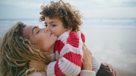 Happy mother cuddling son at autumn ocean shore closeup. Sincere family emotions. Beautiful woman mom closing eyes hugging cute boy outdoors. Adorable curly child kissing parent. Lovely mothers dayの写真素材