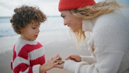 Smiling mom teaching kid at seaside closeup. Cute little boy counting stones resting outdoors in...