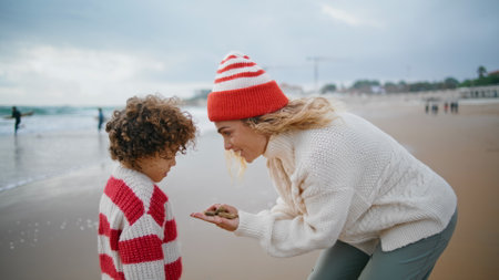 Mother kid playing seaside on autumn weekend. Beautiful woman holding stones talking adorable curly boy at ocean view. Lovely family enjoying creative game resting together. Caring upbringing concept.の写真素材